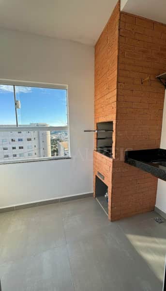 Área externa com churrasqueira de tijolos, pia de granito preto e piso cinza. Janela com vista da cidade.