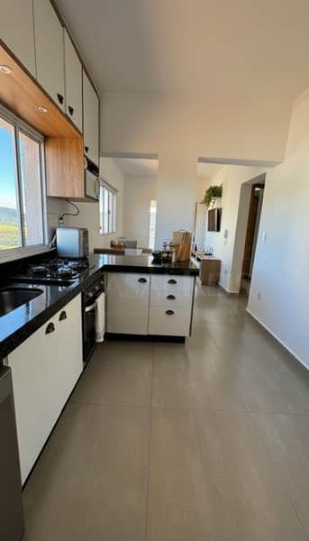 Cozinha moderna com armários brancos e bancada escura. Integração com sala e piso cerâmico claro.