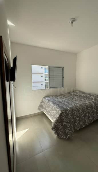 Quarto claro com cama de casal, janela com vista para prédio e piso cinza. Decoração minimalista.
