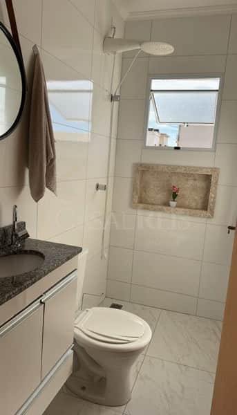 Banheiro claro com pia de granito, vaso sanitário, nicho decorativo e ducha moderna.