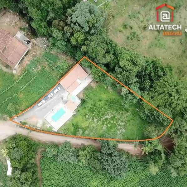 Visão aérea de terreno com casa, piscina e área verde delimitada. Destaque para vegetação abundante.