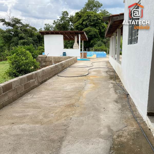 Área externa com piso de concreto, churrasqueira, piscina ao fundo e construção em blocos.