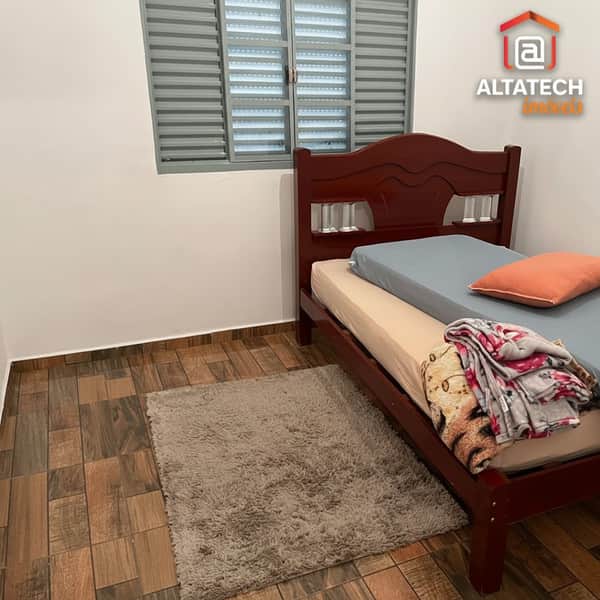 Quarto com cama de madeira, tapete felpudo e janela com persianas. Ambiente aconchegante.