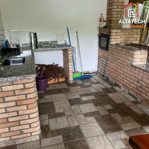 Área externa com churrasqueira de tijolos, pia com bancada de granito e piso cerâmico.