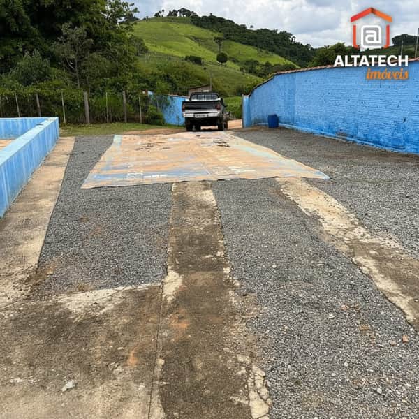 Área externa com balança para caminhão. Terreno amplo com brita e muro azul ao fundo.