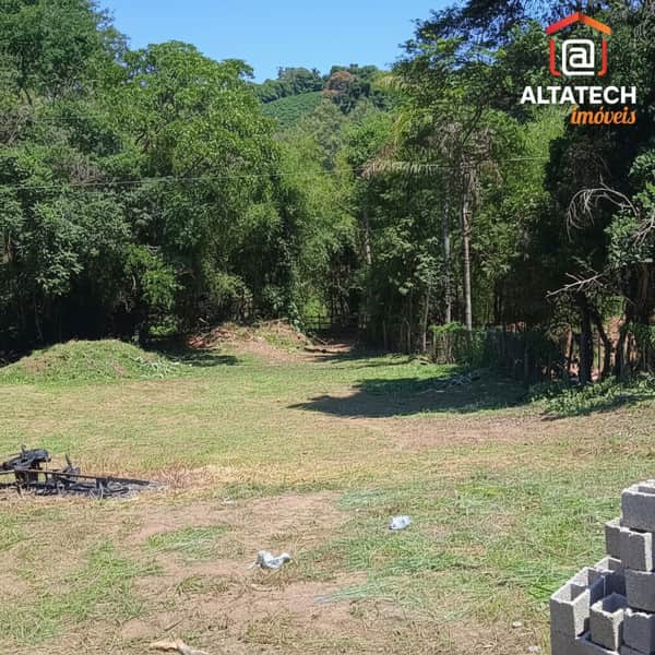 Ampla área externa com gramado, árvores e vegetação. Terreno ensolarado com blocos de construção e churrasqueira.