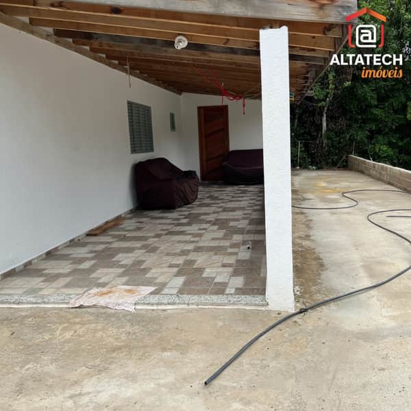 Área externa com piso cerâmico, sofás marrons e coluna branca. Teto de madeira aparente.