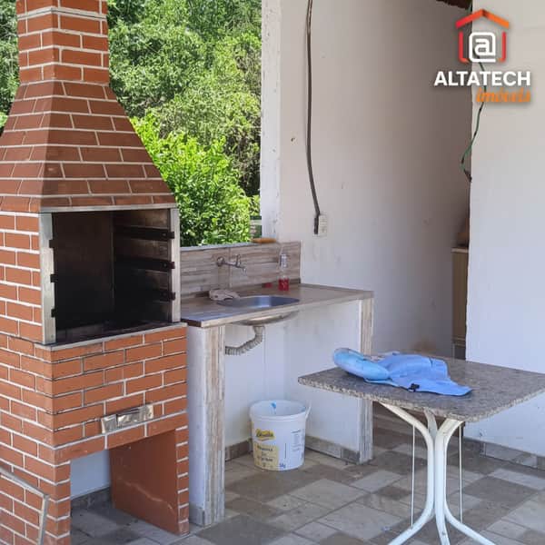 Área externa com churrasqueira de tijolos, pia e mesa. Ambiente amplo e iluminado.