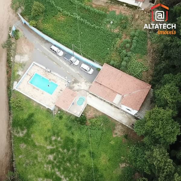Casa com piscina e área externa ampla. Destaque para o telhado rústico e vegetação exuberante.