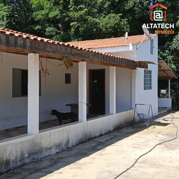 Fachada de casa térrea com varanda, telhado rústico e área externa ensolarada. Detalhes em branco e madeira.