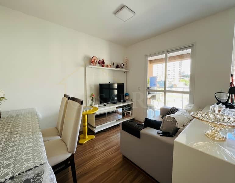 Sala de estar iluminada com TV, sofá cinza, mesa com cadeiras e varanda com vista urbana.