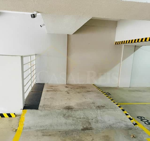 Garagem com vaga demarcada, piso de concreto e detalhes em amarelo e preto. Ambiente iluminado.