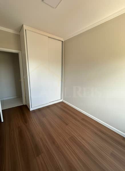 Quarto com piso amadeirado, armário embutido branco e paredes claras. Ambiente iluminado e clean.