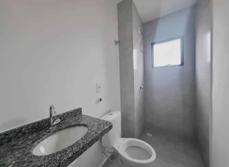 Banheiro claro com pia de granito, vaso sanitário branco e box com revestimento cinza.