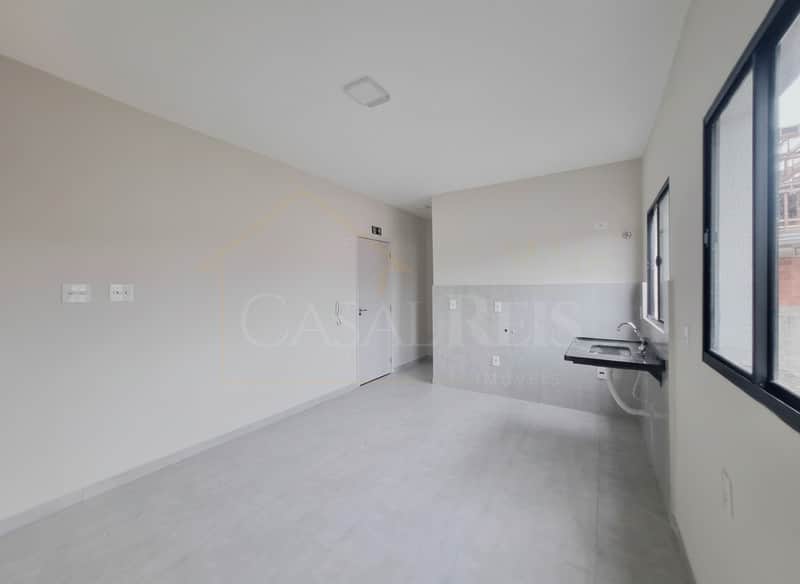 Sala clara com pia e janela grande. Piso cinza, paredes neutras. Espaço amplo e bem iluminado.