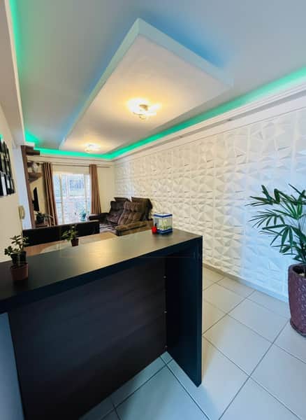 Sala moderna com parede 3D, iluminação verde no teto e balcão preto. Decoração minimalista e elegante.