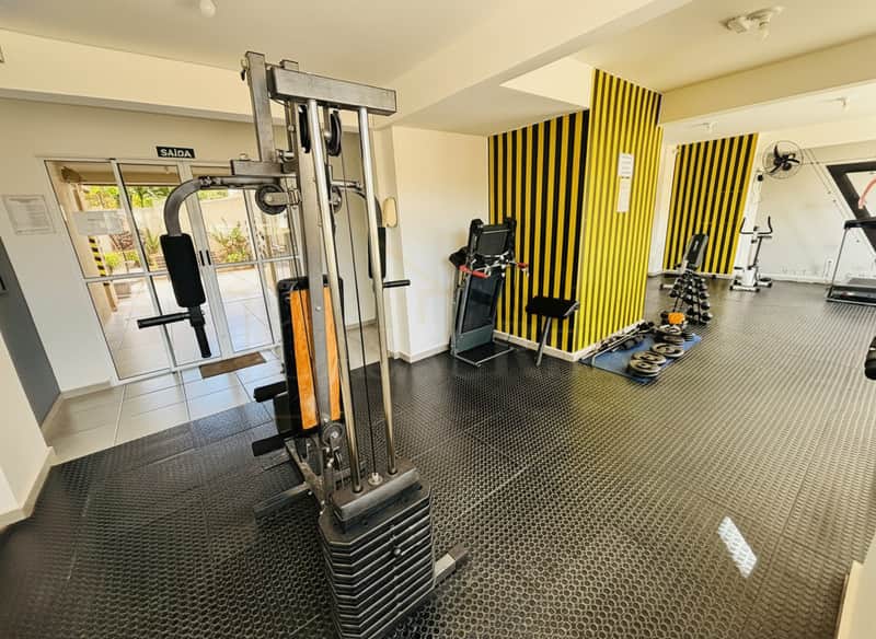 Academia com aparelhos de musculação, esteira e pesos. Paredes listradas em amarelo e preto.