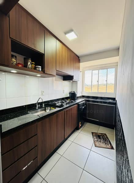 Cozinha moderna com armários marrons, bancada escura, pia de inox e piso cerâmico branco. Janela ao fundo.