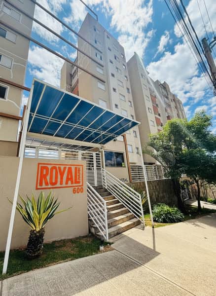 Fachada de edifício residencial com toldo azul, escadas e paisagismo. Destaque para o letreiro "Royal Park 600".