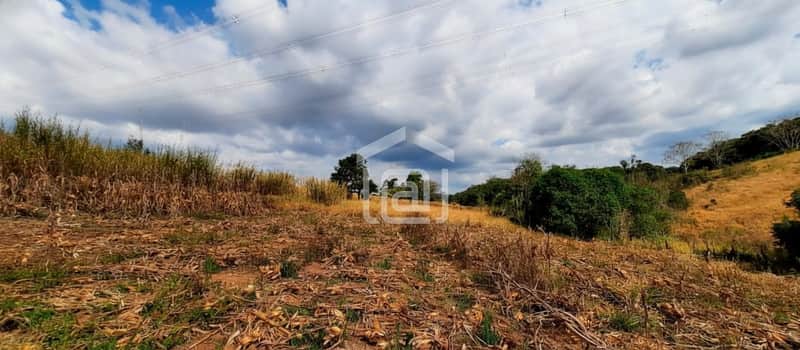 Área externa rural com plantação seca e morro ao fundo. Céu nublado e linhas de energia visíveis.