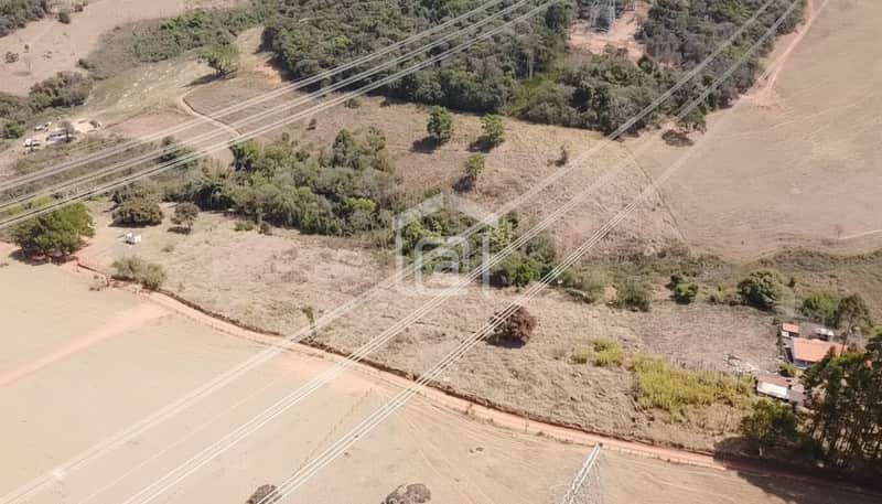 Vista aérea de área rural com pastagem seca e rede elétrica. Vegetação esparsa e construções ao fundo.