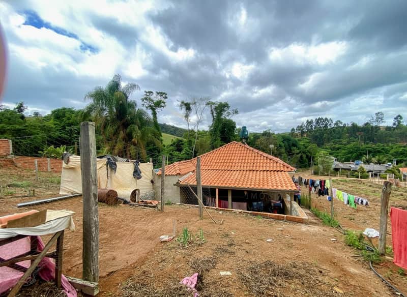 Casa rústica com telhado laranja e área externa. Varal com roupas e vegetação ao fundo.
