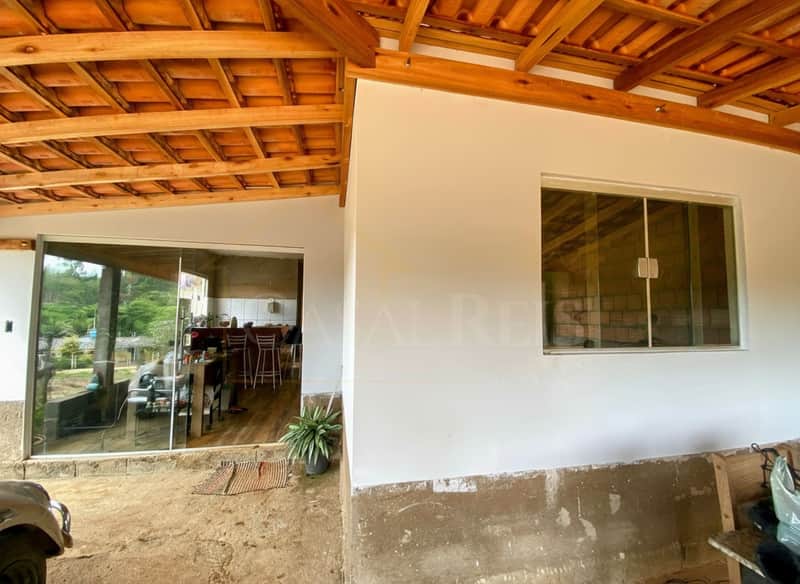 Área externa com janela e porta de vidro, piso rústico e telhado aparente com vigas de madeira.