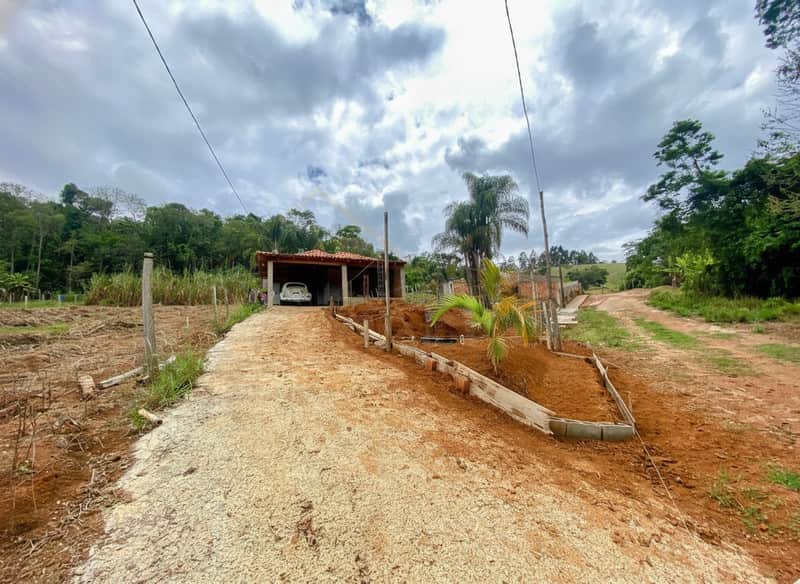 Área externa com casa térrea, carro branco na garagem e paisagismo em construção. Céu nublado.