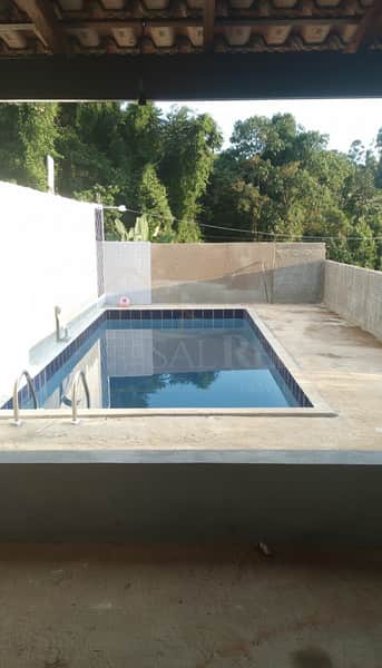Área externa com piscina azul em casa com vista para árvores. Detalhes em azulejo e acabamento em concreto.