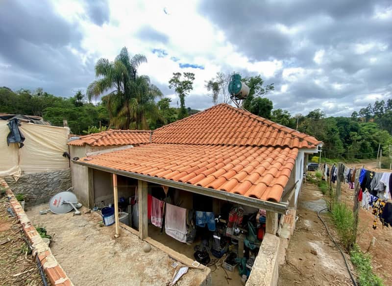 Casa rústica com telhado cerâmico e área externa. Tanque no telhado, roupas no varal.