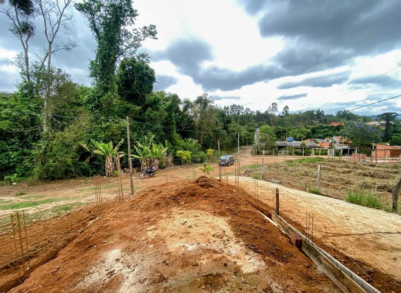 Terreno em construção. Terraplanagem, vegetação ao fundo e céu nublado.