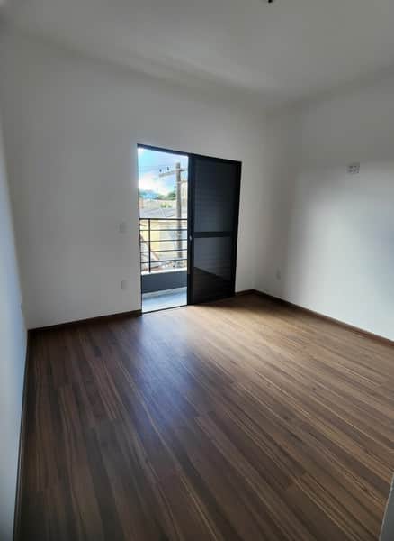 Quarto amplo com piso amadeirado e varanda com porta de correr preta. Ambiente claro e arejado.