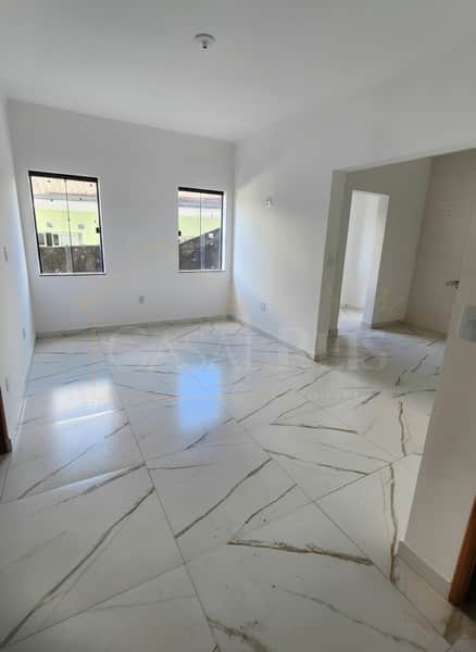 Sala ampla e clara com piso de porcelanato branco e duas janelas. Ambiente arejado e moderno.