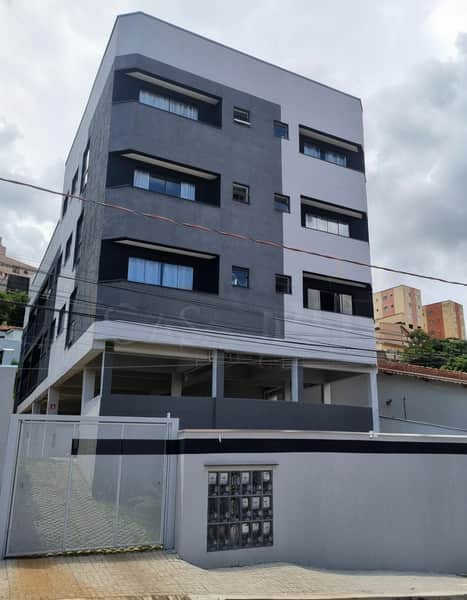Fachada moderna de prédio com janelas e muro cinza. Design minimalista e portão metálico.