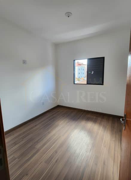 Quarto claro com piso amadeirado e janela. Ambiente arejado, paredes brancas e iluminação natural.