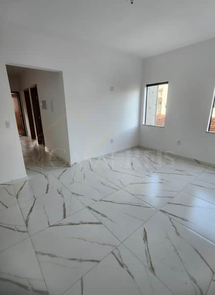 Sala ampla e clara com piso em porcelanato branco e janelas. Ambiente clean e moderno.