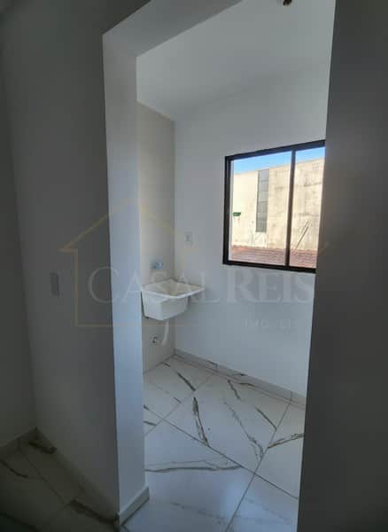 Banheiro pequeno com pia branca, janela e piso de cerâmica clara com veios escuros. Ambiente clean e iluminado.