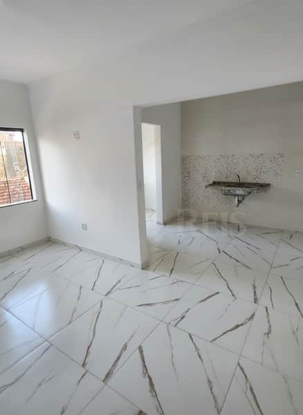 Sala clara com piso em porcelanato, janela e acesso à cozinha com pia.