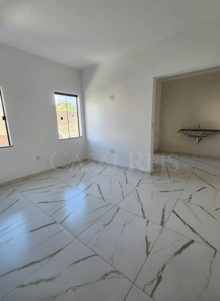 Interior de imóvel com piso marmorizado, paredes brancas, pia e janelas com vista externa.