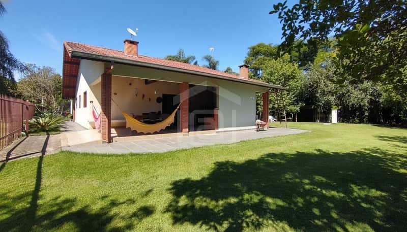 Casa térrea com varanda, jardim gramado e detalhes em tijolo aparente. Área externa ampla e ensolarada.