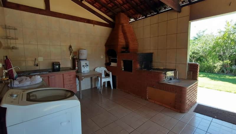 Área externa com churrasqueira de tijolos, pia, máquina de lavar e piso cerâmico. Ambiente amplo e iluminado.