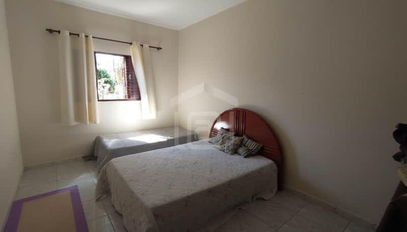 Quarto com duas camas de solteiro, cabeceira de madeira e roupa de cama clara. Janela com cortinas.