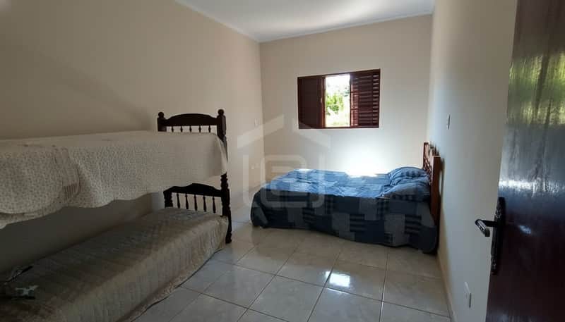 Quarto com beliche de madeira escura e cama de solteiro com colcha azul perto da janela. Piso cerâmico claro.