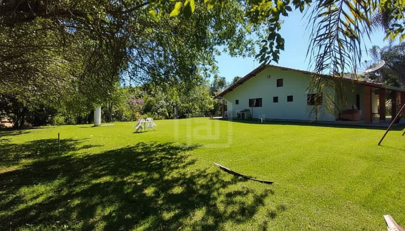 Casa com gramado, árvores e antena parabólica. Área externa ampla e ensolarada em dia de céu azul.