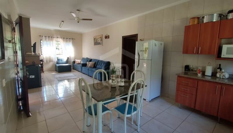 Sala ampla e iluminada com sofá azul, mesa de jantar e cozinha integrada com armários de madeira.