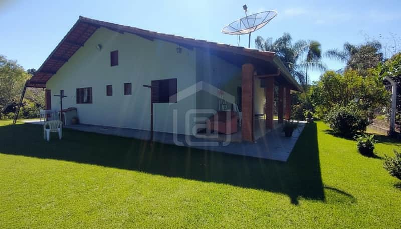 Casa térrea com gramado. Destaque para a fachada com varanda e telhado rústico. Área externa ampla e ensolarada.