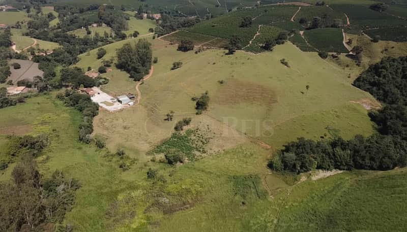 Paisagem rural com pasto verde e área construída. Vista aérea ensolarada de fazenda com vegetação abundante.