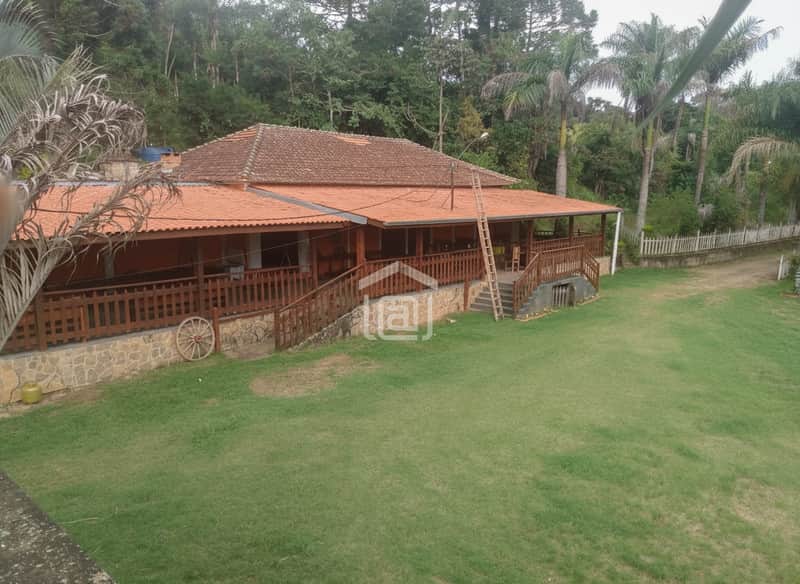 Casa rústica com varanda, telhado de cerâmica e jardim amplo. Destaque para a fachada charmosa e área externa verde.