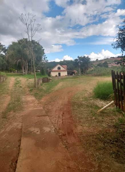 Área externa com casa de campo. Caminho de terra, vegetação e céu azul com nuvens.