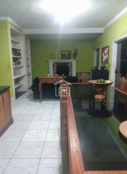 Sala de estar ampla com lareira, estante e mesa de jantar em madeira com tampo de vidro. Decoração clássica.